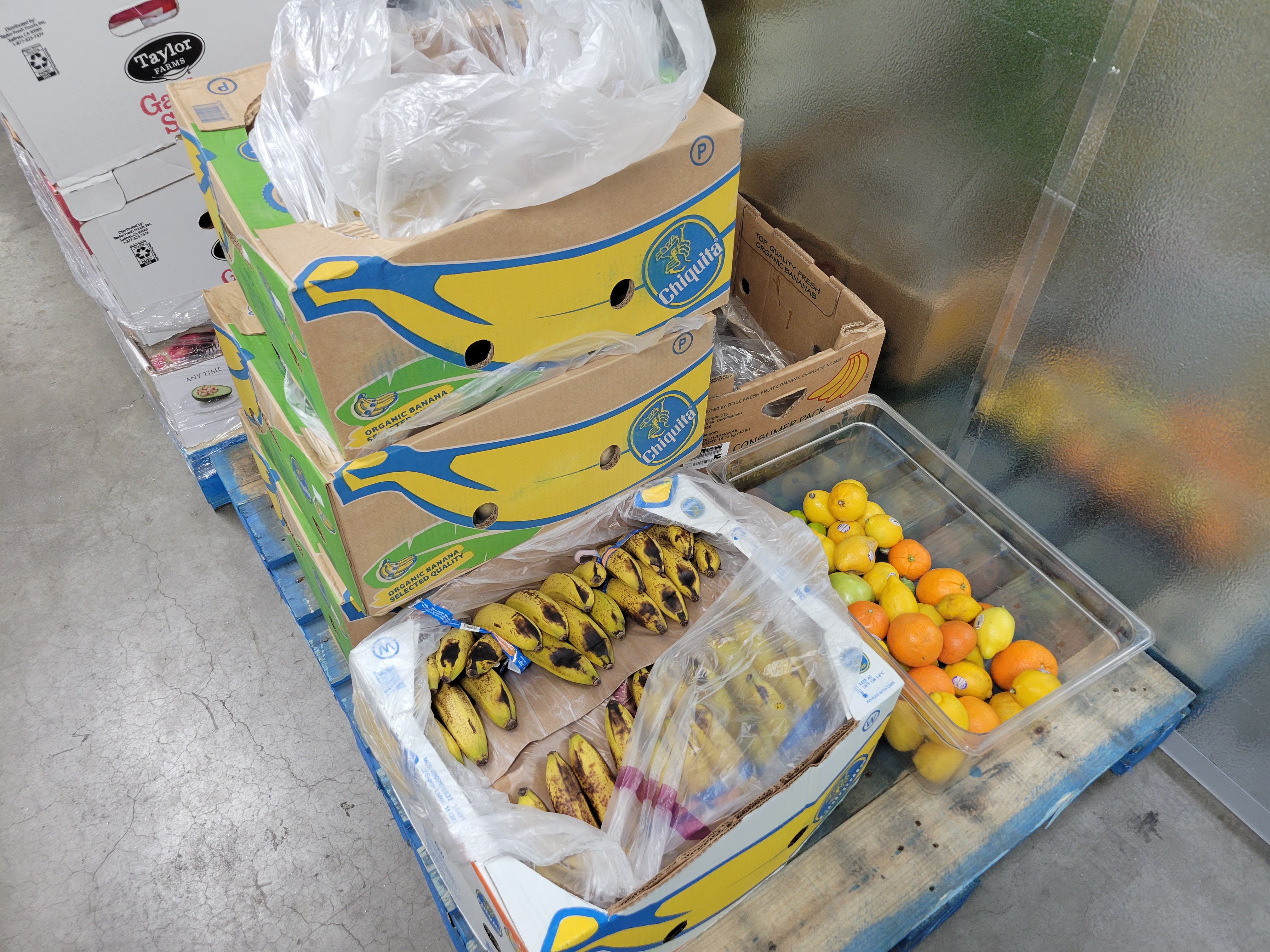 Banana boxes full of bananas and a plastic tub of different fruits on a pallet.